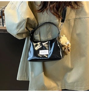 Detail of glossy black patent leather underarm bag with a cute plush bear pendant