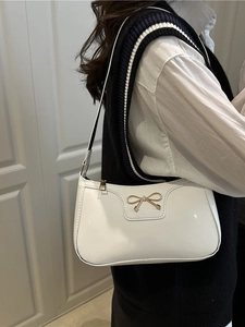 Minimalist white patent leather underarm bag with gold bow clasp on a female model