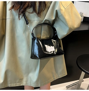 Detail of glossy black shoulder bag with brand label and detachable strap