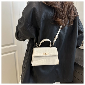 Close-up of a white textured leather crossbody bag with gold hardware worn by a model