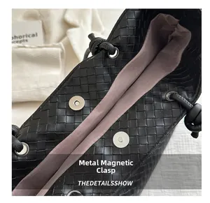 Close-up of black woven leather tote with silver magnetic buckle and purple silk lining