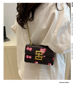Detailed side view of a black cherry print crossbody bag with gold chain on model