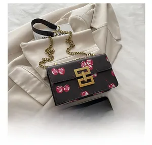 Detail of cherry print on black leather bag with golden geometric clasp and chain strap