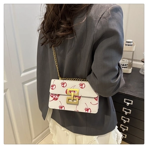 Detail of cherry print handbag with gold buckle and chain strap on a model shoulder
