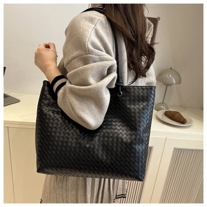 Close-up of black woven leather tote bag texture and slim straps on a fashion model