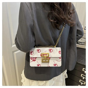 Detail view of white crossbody bag with cherry prints and vintage gold chain strap