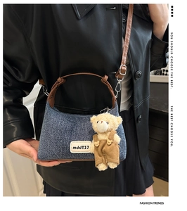 Detail of denim crossbody bag with brown leather handles and a cute plush bear charm