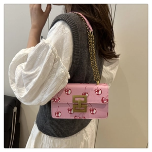 Detail of pink cherry print shoulder bag with gold chain strap worn by a model