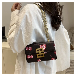Close-up of vintage square bag featuring red cherry prints and golden chain strap detail