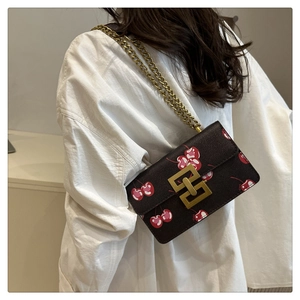 Brown leather crossbody bag with red cherry print and chunky gold chain strap worn by model