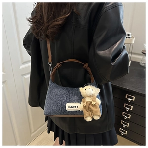 Detail of denim underarm bag with leather trim and a cute plush bear charm accessory