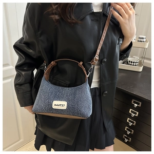 Blue denim dumpling bag with brown leather strap worn by a model in an indoor setting