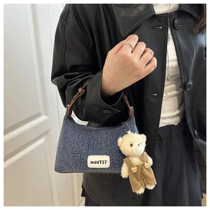 Detail of denim shoulder bag with brown leather strap and cute teddy bear charm