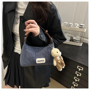 Detail of blue denim crescent bag with leather trim and cute teddy bear charm accessory