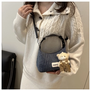 Detail of vintage denim crescent bag with leather handle and cute teddy bear charm