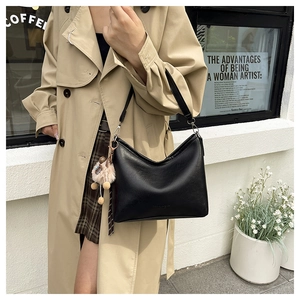 Détail d'un sac sous le bras en cuir noir avec pompon sur un trench-coat beige