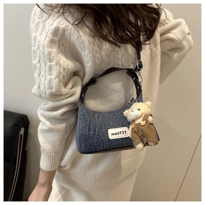 Detail of blue denim hobo bag with teddy bear pendant worn by model in cozy sweater