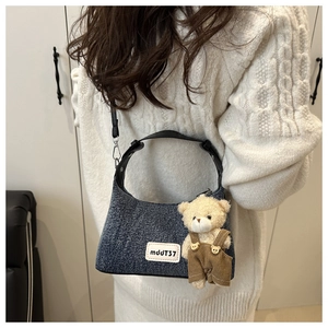Detail of blue denim shoulder bag with brown bear plush toy and leather logo label