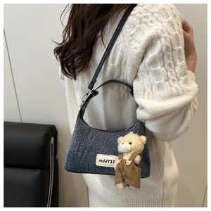 Detail of blue denim shoulder bag featuring a mini plush bear charm and woven logo tag