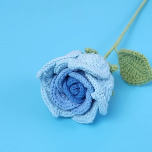 Close-up of handmade crochet Thai rose in gradient blue with green leaves and stem