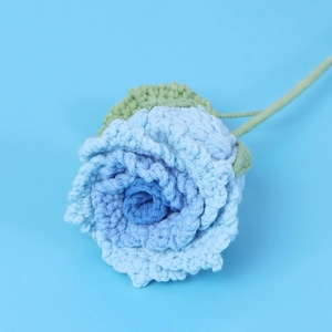 Macro view of blue gradient handmade crochet rose with textured yarn petals and green leaf