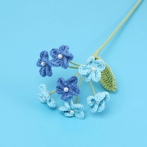 Detail of handcrafted crochet blue flowers with white pearl centers and green leaves