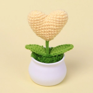 Close-up of handmade crochet yellow heart potted plant with green leaves and white pot