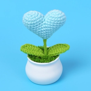 Macro shot of handmade crochet heart potted plant with intricate yarn texture on blue base