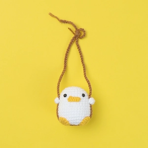 Handmade crochet white duck car mirror hanging ornament with yellow beak on yellow backdrop