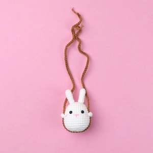 Close-up of handmade white crochet rabbit pendant with long brown cord on pink background