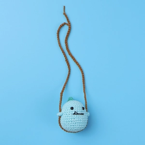 Detail of a handmade blue crochet duck charm featuring a green hat on a blue background
