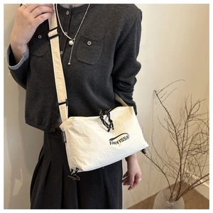 Detail of cream nylon crossbody bag featuring adjustable strap and branded logo tag