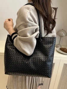 Black hand-woven leather tote bag with minimalist shoulder straps in a lifestyle setting