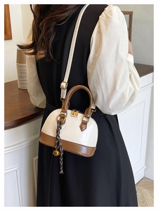 Close-up of a classic shell-shaped crossbody bag with gold zippers and tassel detail