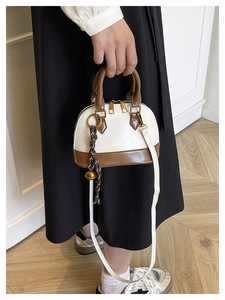 Detailed view of bicolor shell bag with brown top handle and decorative beaded tassel