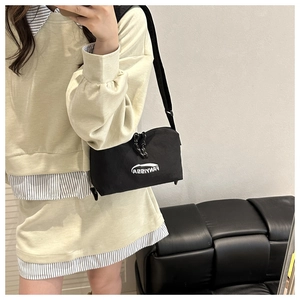 Selfie miroir montrant un sac bandoulière en nylon noir avec logo blanc et tirette tressée