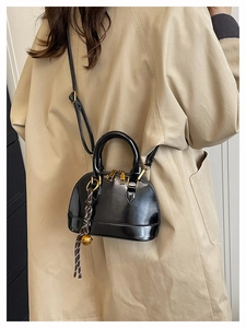 Close-up of black patent leather shell bag with gold hardware and woven bell charm