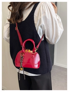 Detail of red shell crossbody bag with golden dual zippers and woven bell charm accessory