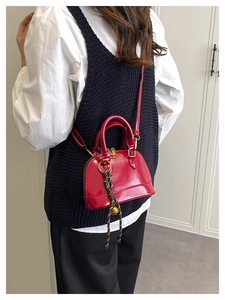 Detail of red shell dome bag featuring a glossy finish and a gold bell decorative charm