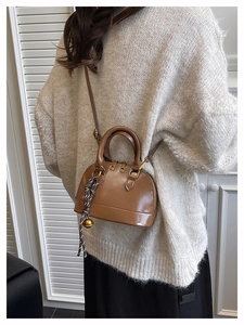 Detail of a brown shell handbag with gold hardware and woven pendant on a knit sweater
