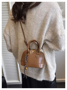 Detail of brown mini shell bag in shiny PU leather with woven charm on beige sweater