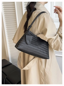 Dettaglio ravvicinato di una borsa a tracolla in pelle intrecciata nera con trench color kaki