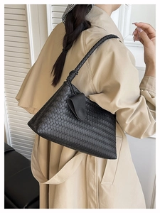 Dettaglio di una borsa a spalla intrecciata nera con texture in pelle su un cappotto beige