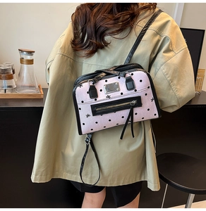 Close-up of pink polka dot crossbody bag with black leather straps and metal nameplate