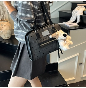 Close-up of black polka dot denim tote with silver zipper and white plush dog charm