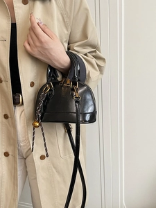 Chic black glossy shell bag with gold hardware and woven charm shown with a trench coat