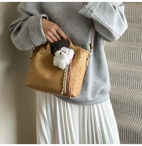 Detail of camel woven bucket bag with plush dog charm shown on model in stairwell