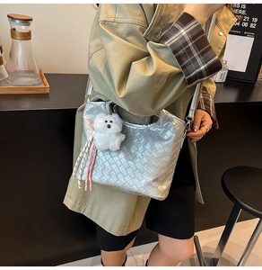 Detail of silver woven crossbody bag with metallic texture, plush bear and tassel charm