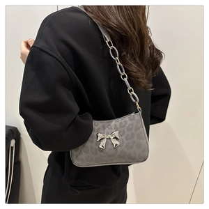Close-up of grey leopard baguette bag featuring a silver bow and chain strap on model