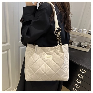 Detail of cream quilted tote bag featuring gold chain strap and metallic brand logo